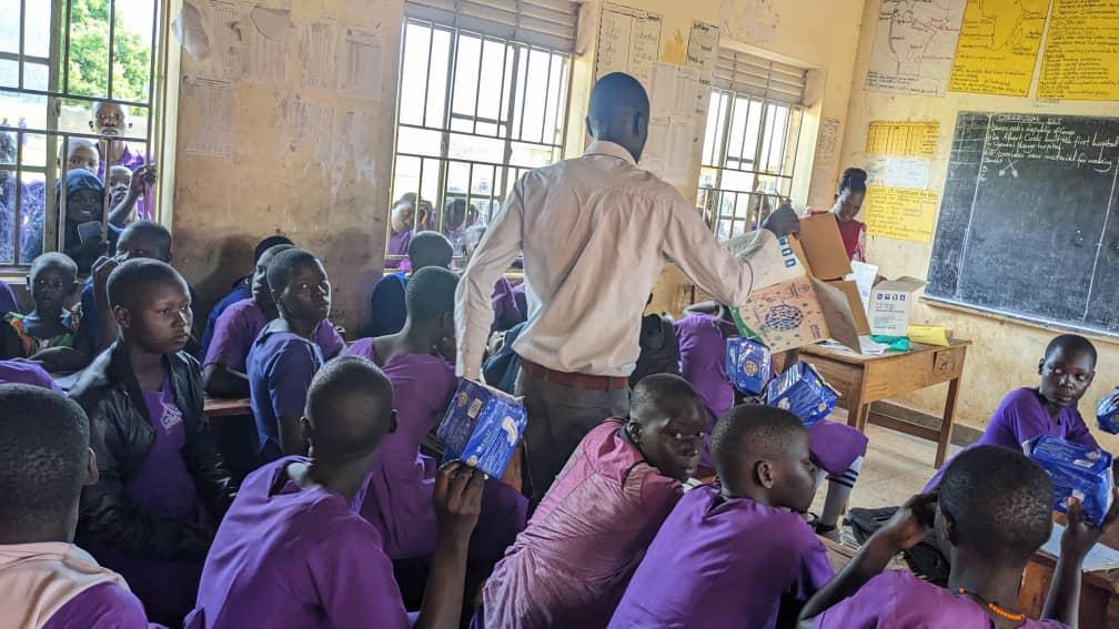 Girls in purple uniforms proudly holding Freedom sanitary pads after distribution in Napak, Karamoja