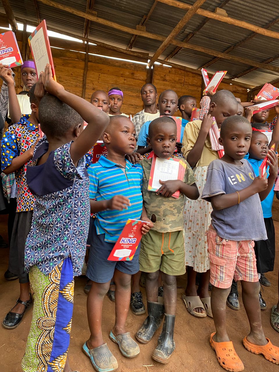 Young children proudly holding their KING exercise books after receiving them