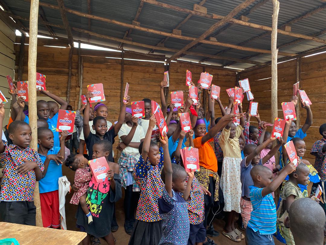 Children of all ages gathered together holding their exercise books high in Banda slum